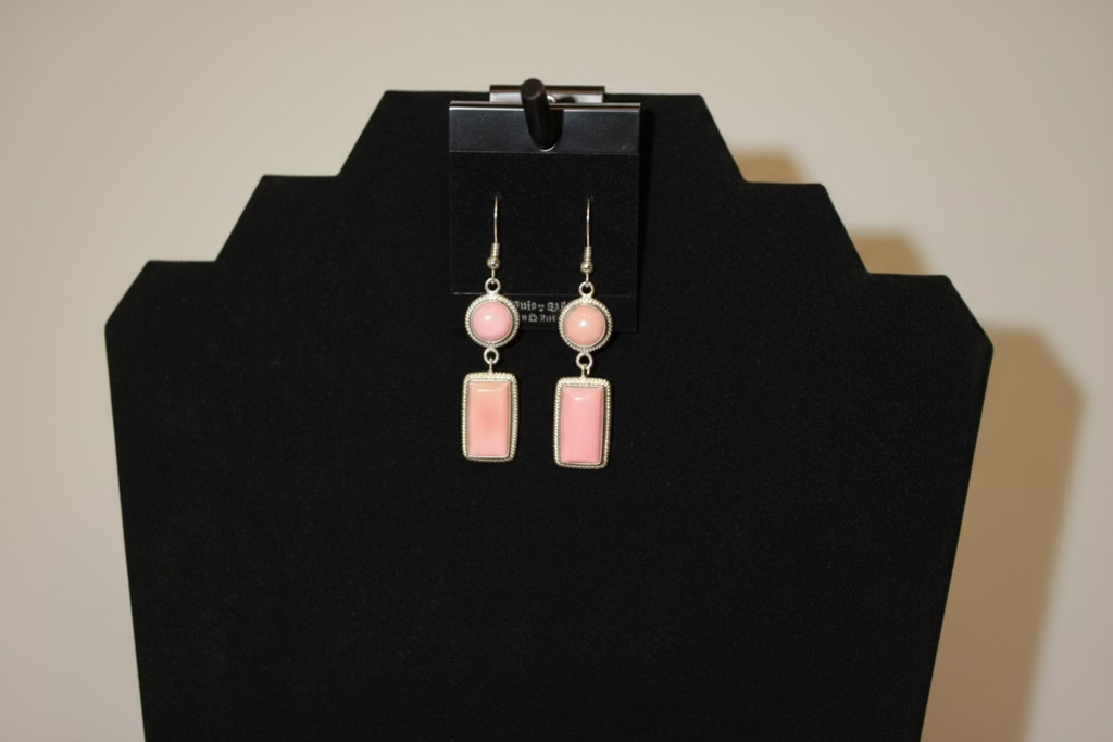 Pink earrings on a black jewelry display stand against a white background