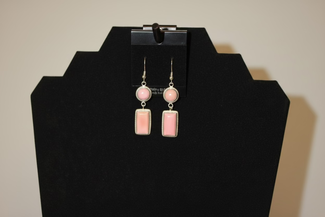 Pink earrings on a black jewelry display stand against a white background